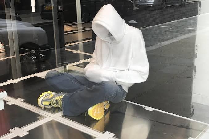 Seated figure in a white hoodie, Selfridges
